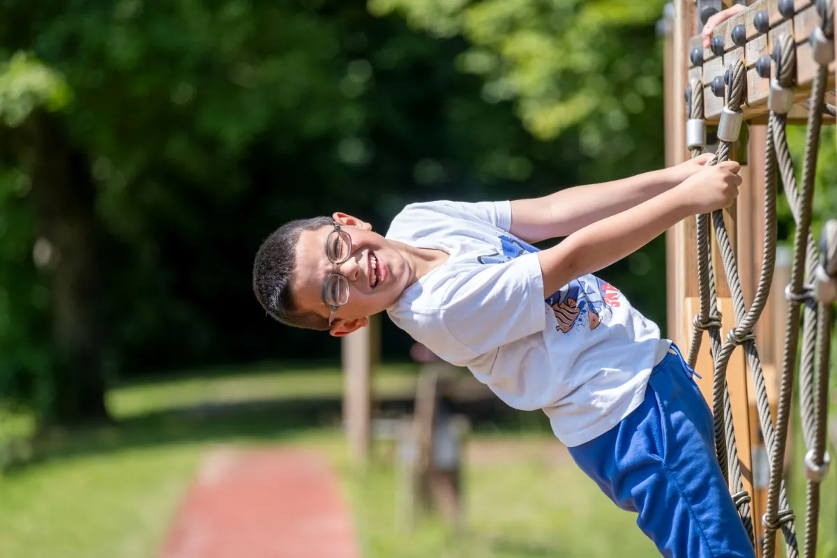 Junge klettert auf Klettergerüst im Garten und lacht